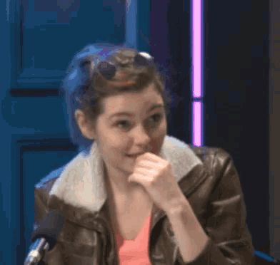 a woman wearing a brown leather jacket is laughing in front of a microphone