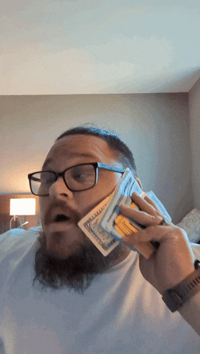 a man with glasses is holding a stack of 20 dollar bills in front of his face