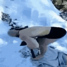 a man without a shirt is bending over in the snow with a hammer .