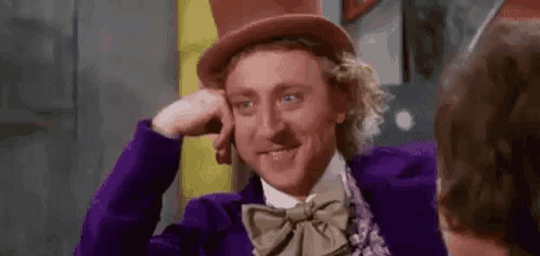 a man in a top hat and bow tie is smiling while talking to another man .