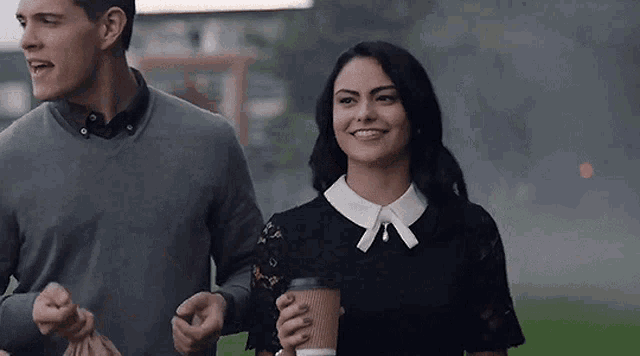 a man and a woman are walking together and the woman is holding a coffee cup .