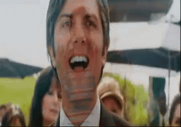 a man in a suit and tie is making a funny face while standing in front of a crowd .
