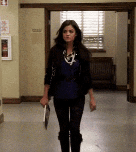 a woman is walking down a hallway holding a folder