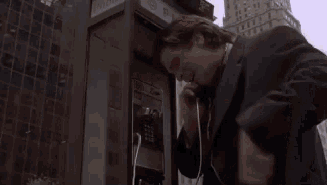 a man in a suit is talking on a cell phone in a pay phone booth .