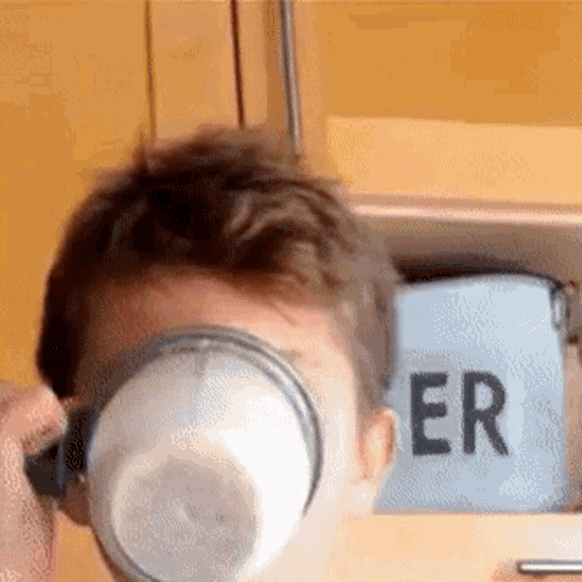 a man is holding a cup in front of his face in front of a bag that says er
