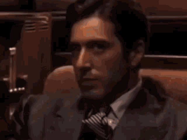 a man in a suit and tie is smoking a cigarette and looking at the camera .
