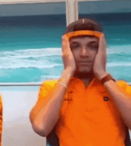 a man wearing an orange shirt and a headband covering his face with his hands