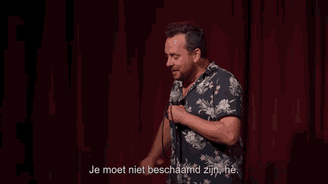 a man stands in front of a microphone and says je moet niet beschaamd zijn he