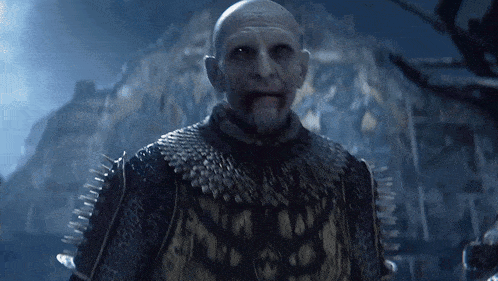 a bald man with a beard is wearing a black and gold outfit with spikes on the sleeves