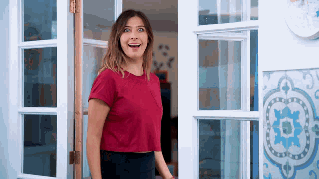 a woman in a red shirt stands in front of a white door