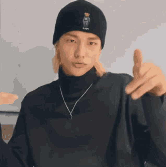 a young man wearing a black beanie and a black turtleneck is standing in front of a white board .