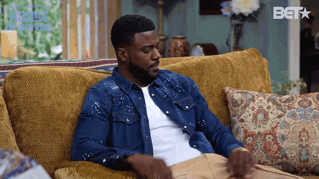 a man in a denim shirt is sitting on a couch with a bet logo in the background