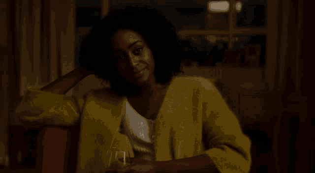 a woman in a yellow sweater is sitting in a chair holding a glass