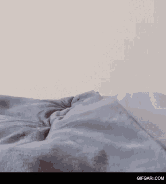a person is laying on a bed with a gray blanket on it .
