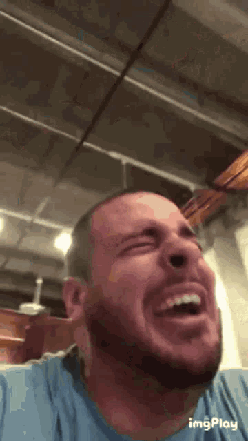 a man with a beard is laughing with his mouth open in a room .