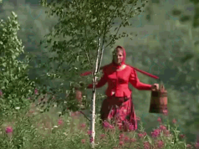a woman in a red dress and head scarf is holding a tree trunk .