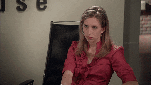 a woman in a red shirt sits in a chair in front of a wall with the letters s and e on it