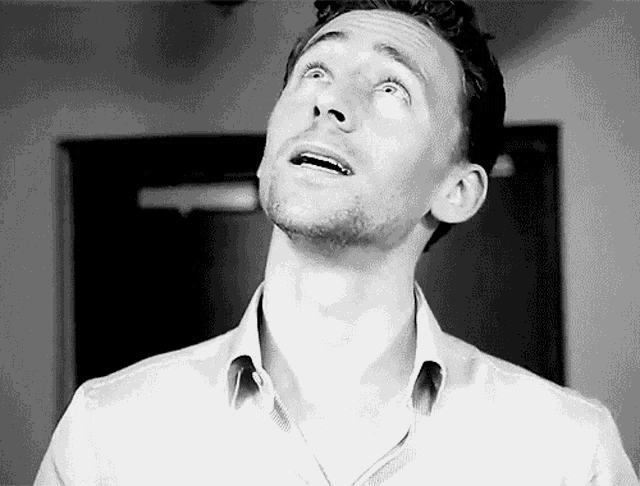 a man with a beard and a white shirt is looking up at the sky in a black and white photo .