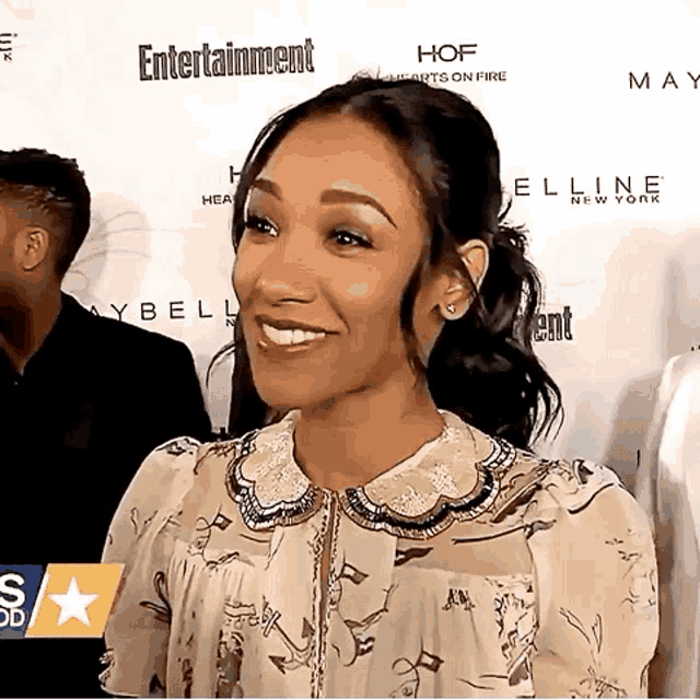 a woman is smiling in front of a wall that says entertainment