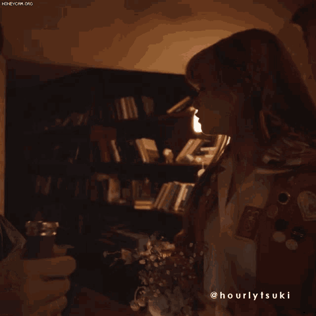 a woman in a red jacket is standing in front of a bookshelf with the name hourlytsuki on her shirt