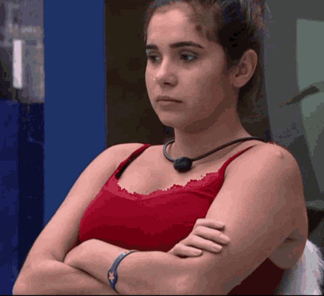 a woman in a red tank top has her arms crossed and a necklace around her neck