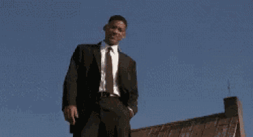 a man in a suit and tie is standing on the roof of a building giving the middle finger .