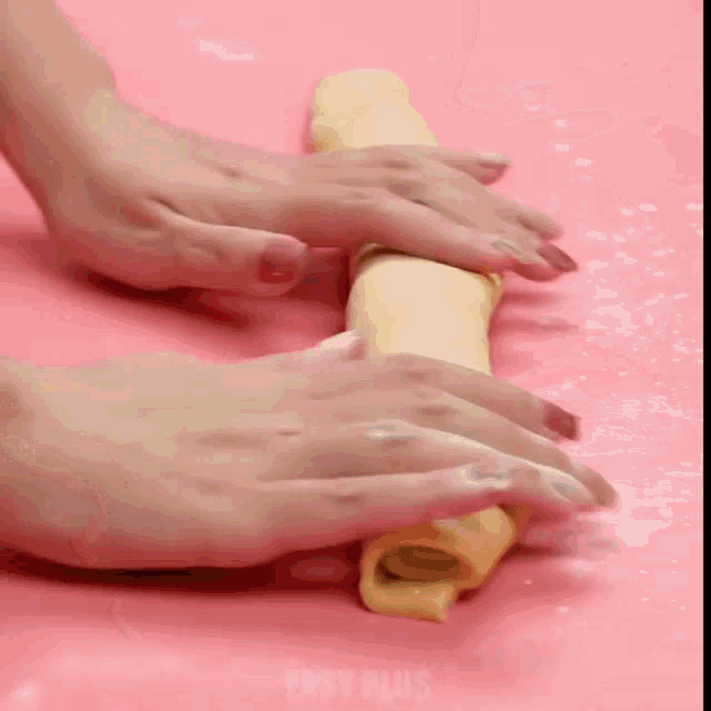 a person is rolling a piece of dough on a pink surface that says enjoy plus