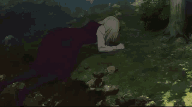 a woman is kneeling on the ground in the woods .