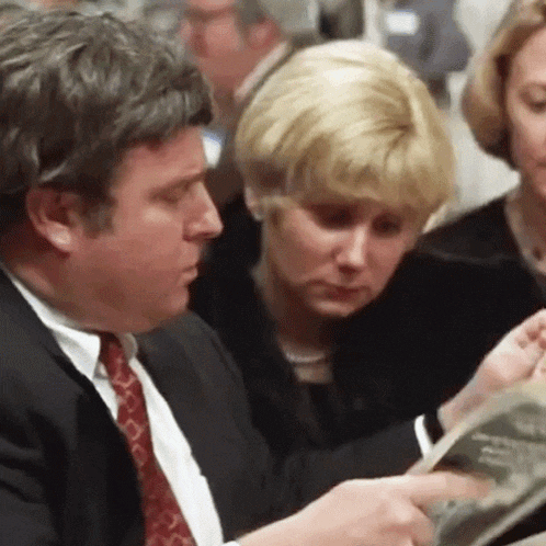 a man in a suit and tie is reading a book to a woman