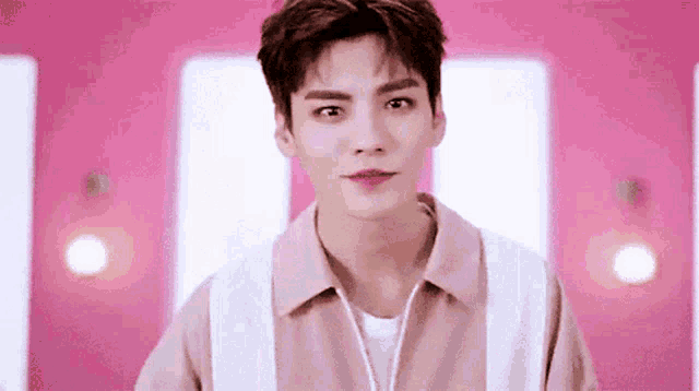 a young man in a pink shirt and white vest is standing in front of a pink wall .