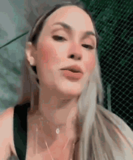 a woman with long blonde hair is wearing a black tank top and a necklace .