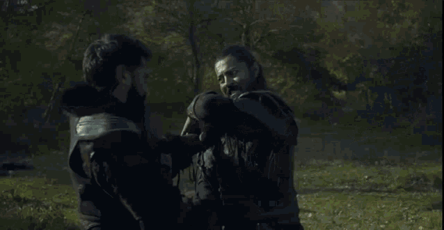 a man is laying on the ground in the woods with a sword .