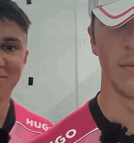a man wearing a pink shirt with the word hug on it is standing next to another man wearing a hat .