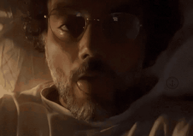 a man with glasses and a beard is laying in a dark room