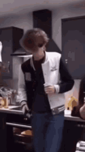 a man in a black and white jacket is standing in a kitchen holding a cup