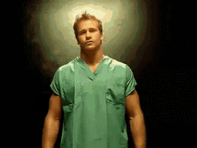 a man in a green scrub top stands in front of a dark background