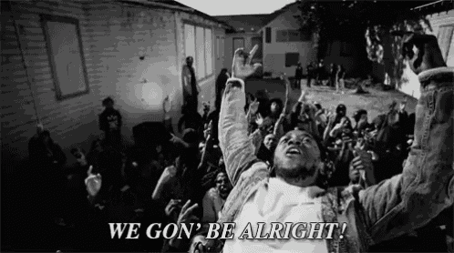 a man is standing in front of a crowd with his arms in the air and the words we gon ' be alright .