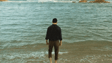 a man in a black shirt is standing on the beach looking at the ocean