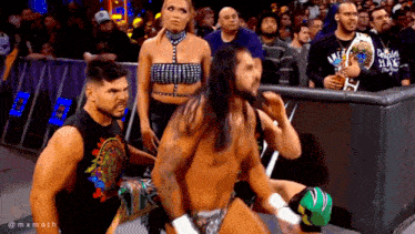 a group of wrestlers are standing in front of a crowd while a woman watches .