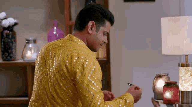 a man in a yellow sequined shirt is writing with a pen