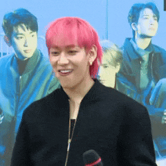 a young man with pink hair is talking into a microphone