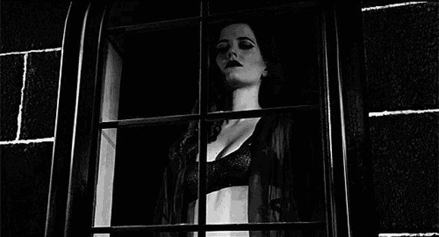 a black and white photo of a woman looking out of a window .
