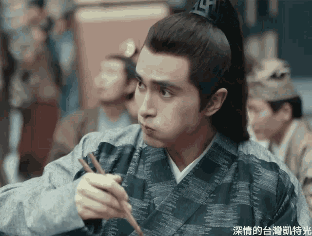a man wearing a ponytail is holding chopsticks in his hand