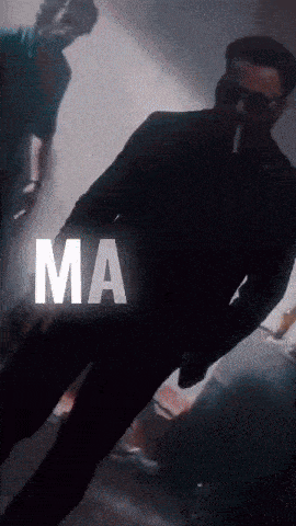 a man in a suit is smoking a cigarette and the word ma is on the bottom right