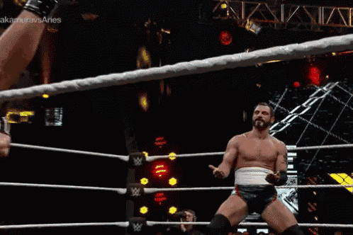 a man without a shirt is standing in a wrestling ring with his hands outstretched .