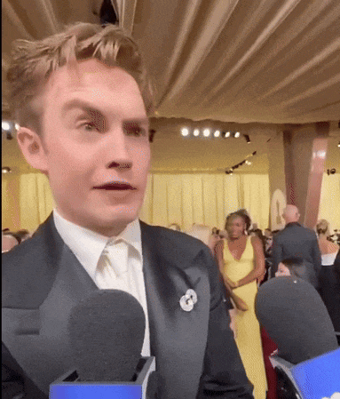 a man in a tuxedo is talking into a microphone at a party
