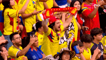 a man wearing a scarf that says ' colombia ' on it stands in a crowd of people