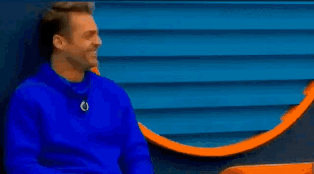 a man in a blue sweater is laughing and leaning against a wall .