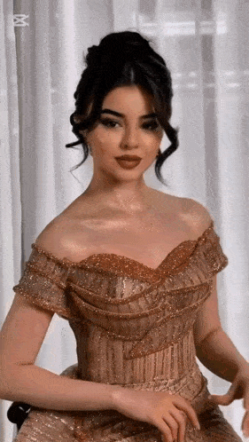 a woman in a gold off the shoulder dress is sitting in front of a white curtain