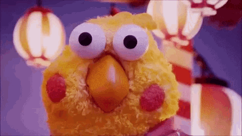 a stuffed yellow bird with big eyes is standing in front of some lanterns